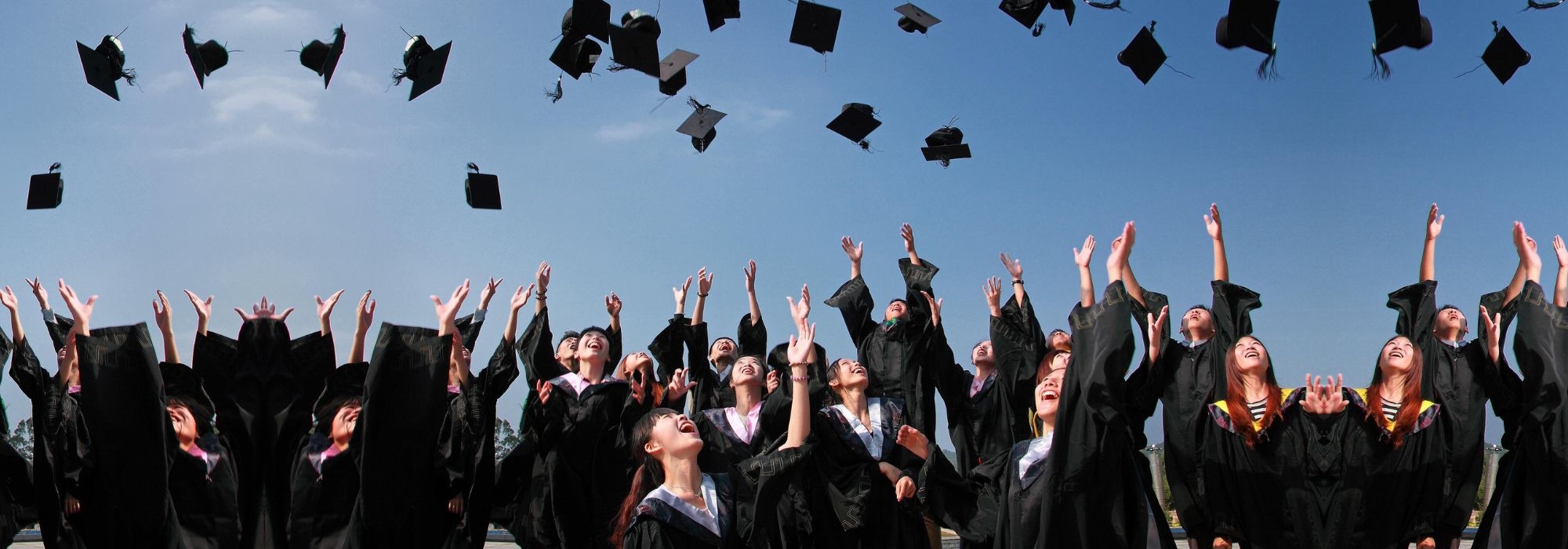 A group of young people in graduating gowns throwing their caps in the air.