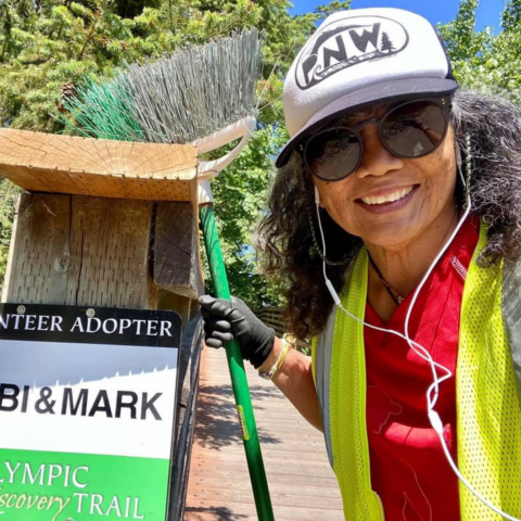 Woman holding broom standing next to a trail marker