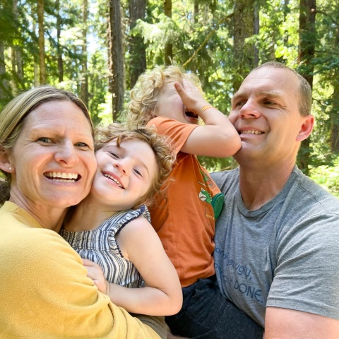 Woman, man, young girl and young boy standing in a forest smiling