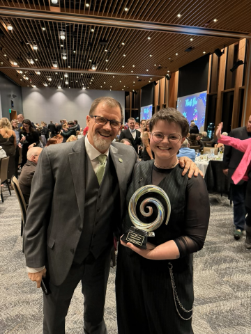 Two people smiling while one holds an award