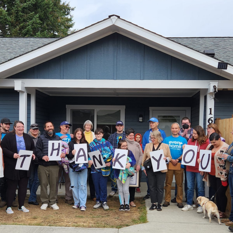 A group of people in front of a house holding signs reading "thank you"