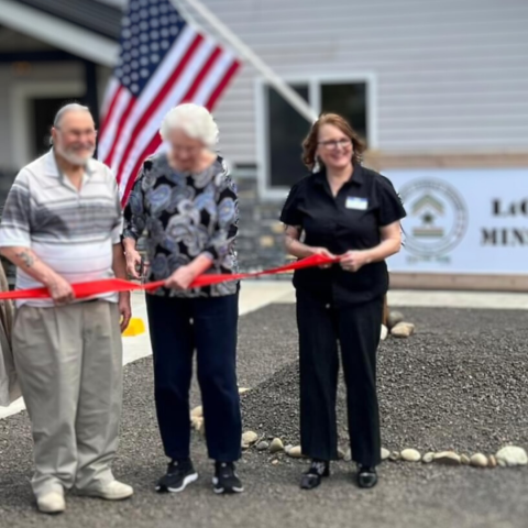 people cutting a ribbon in front of a house